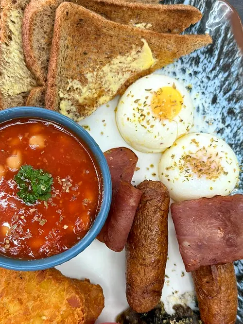 An English-style breakfast at Rumi: soft-poached eggs, turkey rashers, chicken sausages, a hash brown, baked beans in a bowl and buttered wholemeal toast.