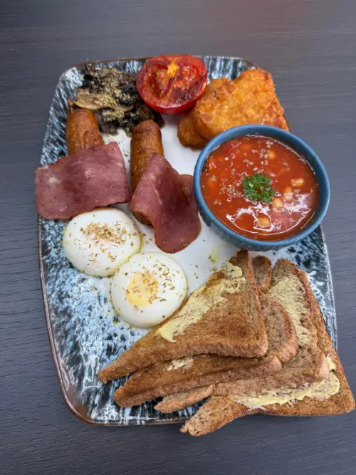 A second English-style breakfast plate: poached eggs, turkey rashers, sausages, hash brown, mushrooms, roasted tomato, beans and toast.