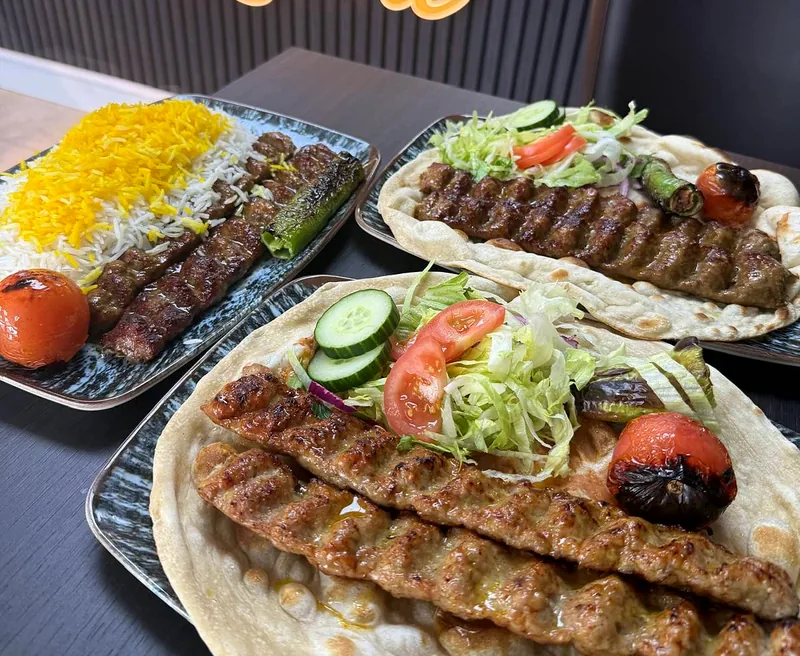 Koobideh at Rumi: minced lamb and saffron chicken skewers on flatbread with grilled tomato and a dressed salad, beside saffron rice.